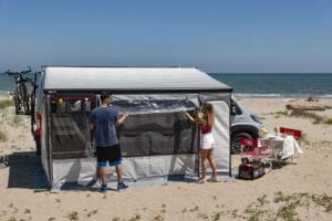 Fiamma Privacy Room onder een camperluifel op het strand, voorpaneel half opgerold