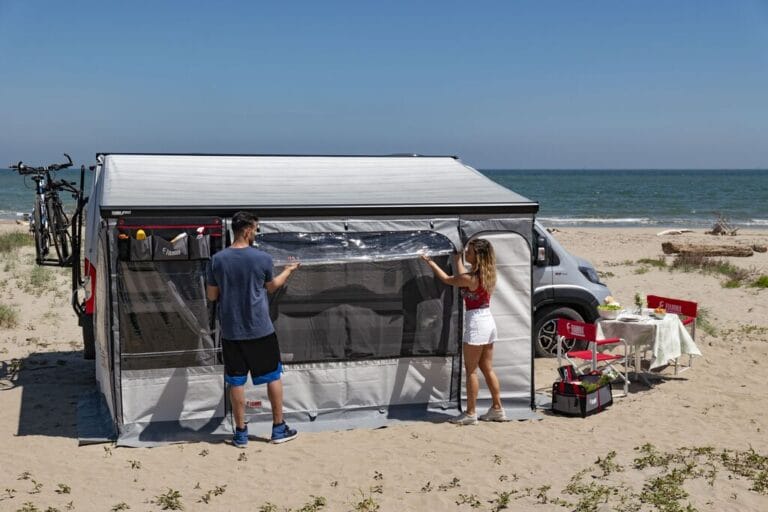 Fiamma Privacy Room onder een camperluifel op het strand, met het voorpaneel half opgerold