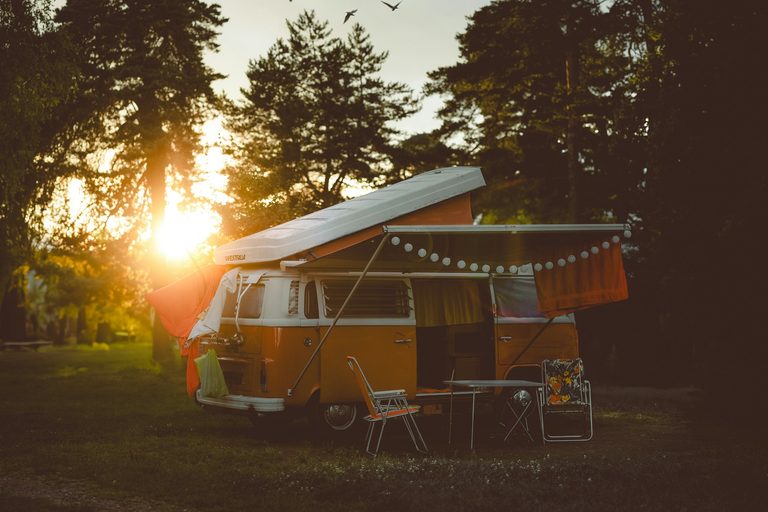 Benodigdheden camper: buscamper met opklapdak op de camping, met luifel, lichtjes, campingstoelen en een klaptafel