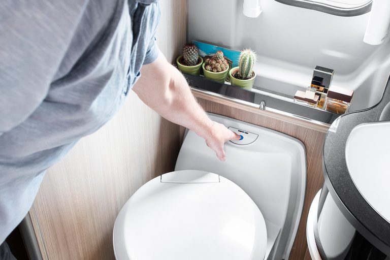 Chemisch toilet in de camper: iemand drukt op de spoelknop van een Thetford-cassettetoilet in een camperbadkamer