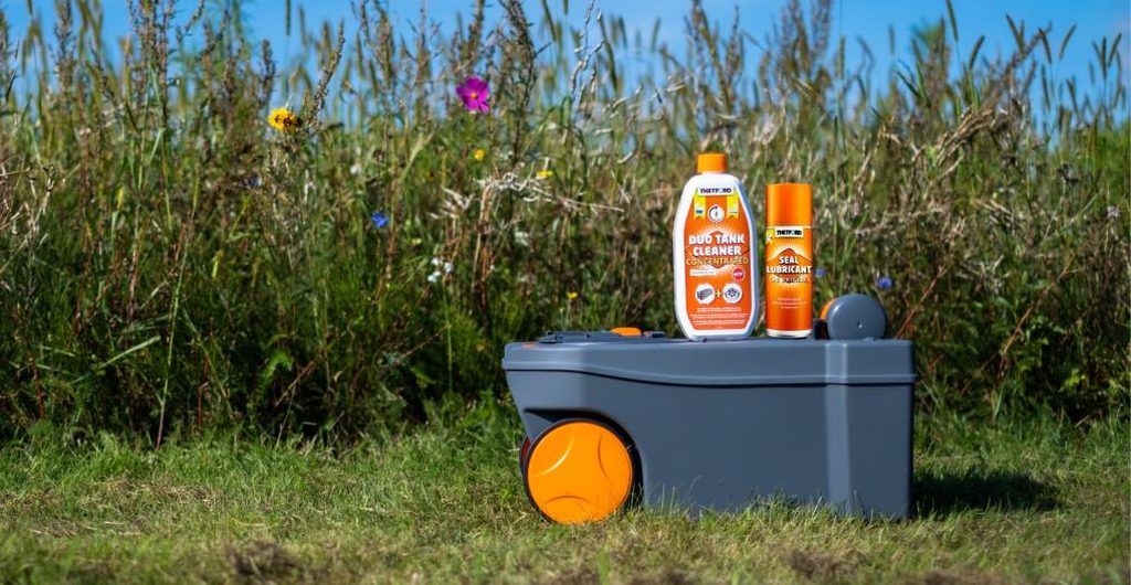 Chemisch toilet reinigen: cassette van een Thetford-cassettetoilet in het gras met een fles Duo Tank Cleaner en een spuitbus Seal Lubricant erop