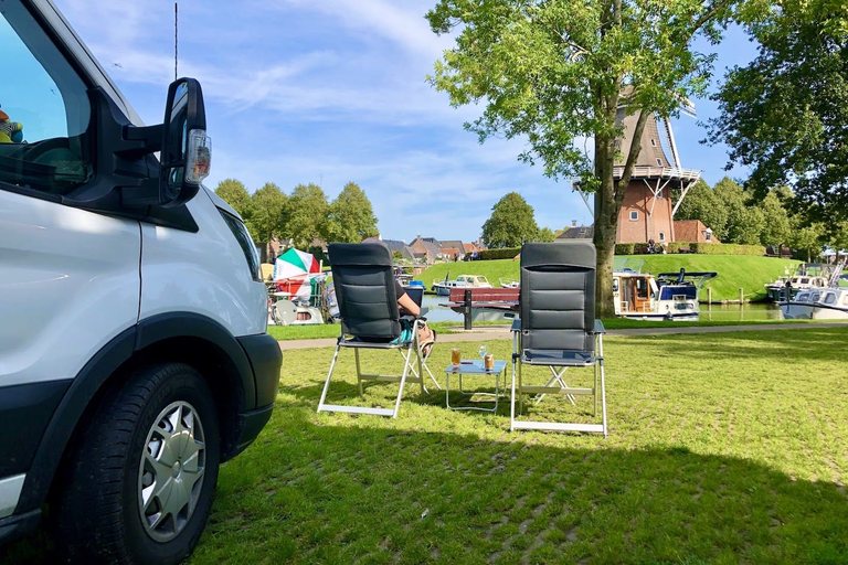 Twee Dukdalf campingstoelen op het gras naast een camperbus, aan een haven met een molen