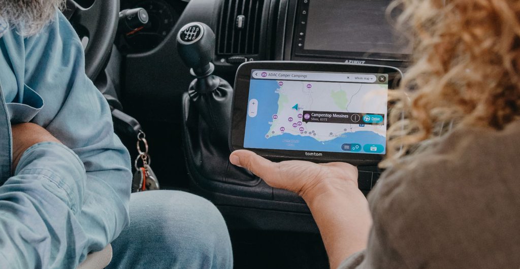 Bijrijder houdt de TomTom GO Camper Max vast met de kaart van ADAC-camperplaatsen in Portugal op het scherm