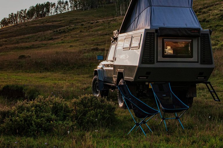 Twee lichtgewicht campingstoelen achter een terreinwagen met camperopbouw bij zonsondergang