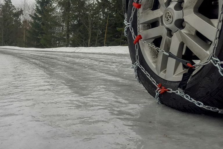 Sneeuwkettingen verplicht: sneeuwketting om het voorwiel van een auto op een ijzige weg