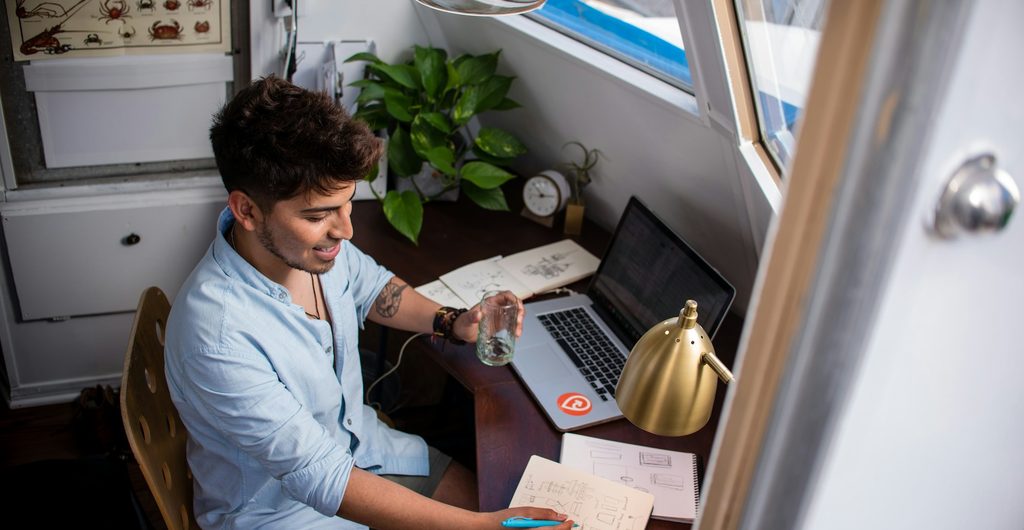 Man werkt aan een laptop aan het tafeltje in een camper, met het raam open