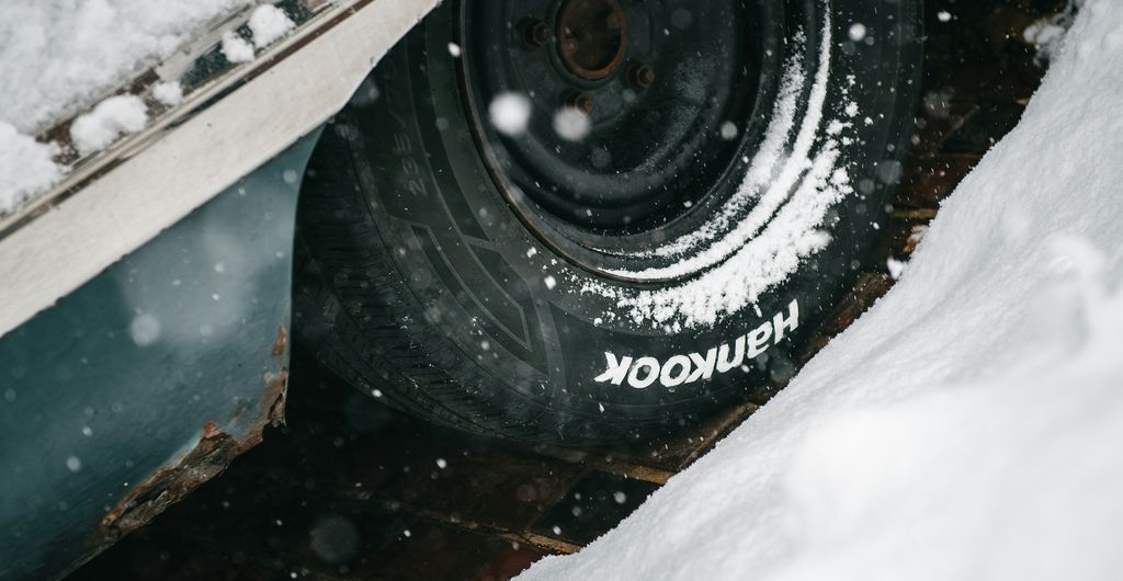 Winterband met profiel vol sneeuw in de wielkast van een auto, met sneeuwvlokken in de lucht