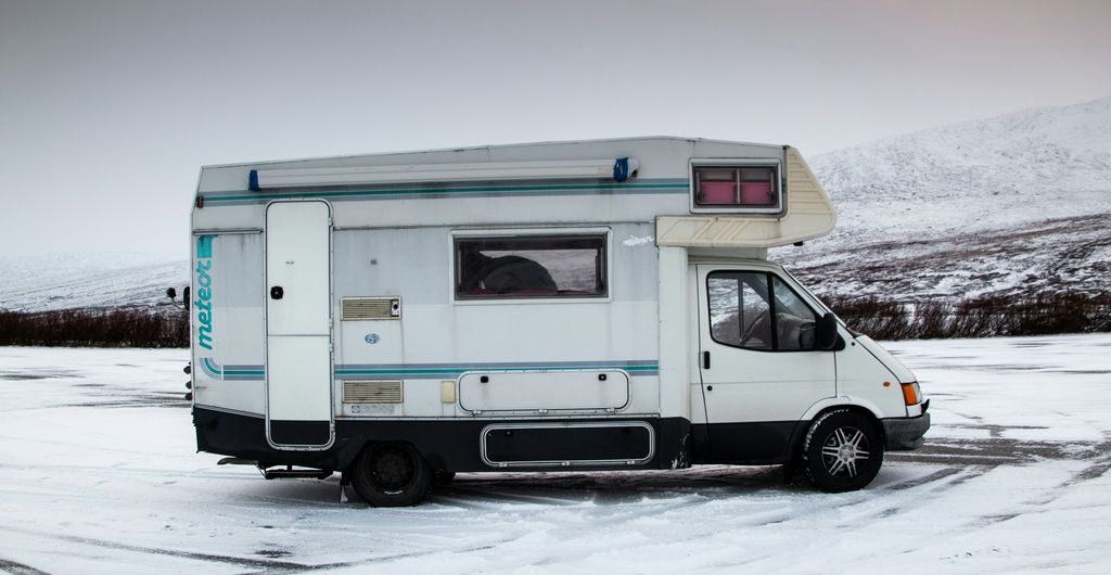 Alkoofcamper op een besneeuwde parkeerplaats in de bergen, klaar voor een rit met winterbanden