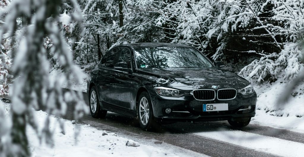 Een auto met winterbanden op een besneeuwde bosweg in Duitsland, met sneeuw op de takken langs de weg