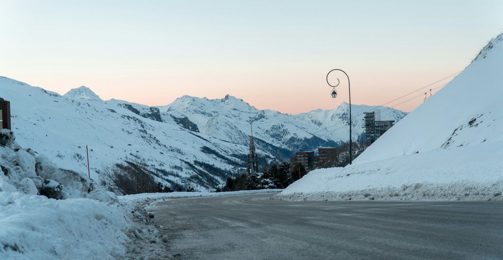 Winterbanden Frankrijk: weg door Les Menuires in de Savoie, met sneeuw langs de kant en besneeuwde bergen bij zonsondergang