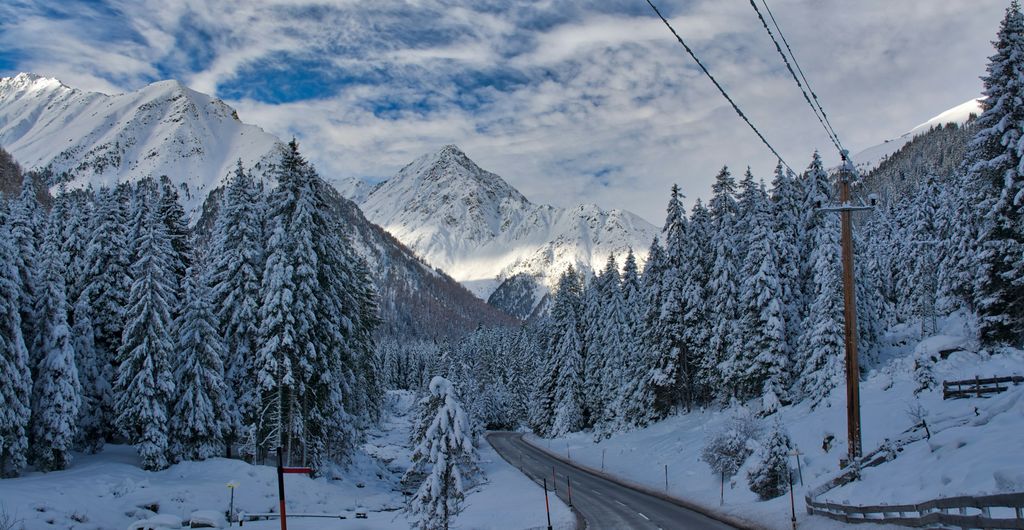 Winterbanden Oostenrijk: weg door een besneeuwd bos bij K&uuml;htai in Tirol, met sneeuw op de bomen en in de berm